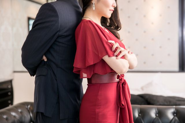 背中を合わせるスーツの男性と赤いドレスの女性